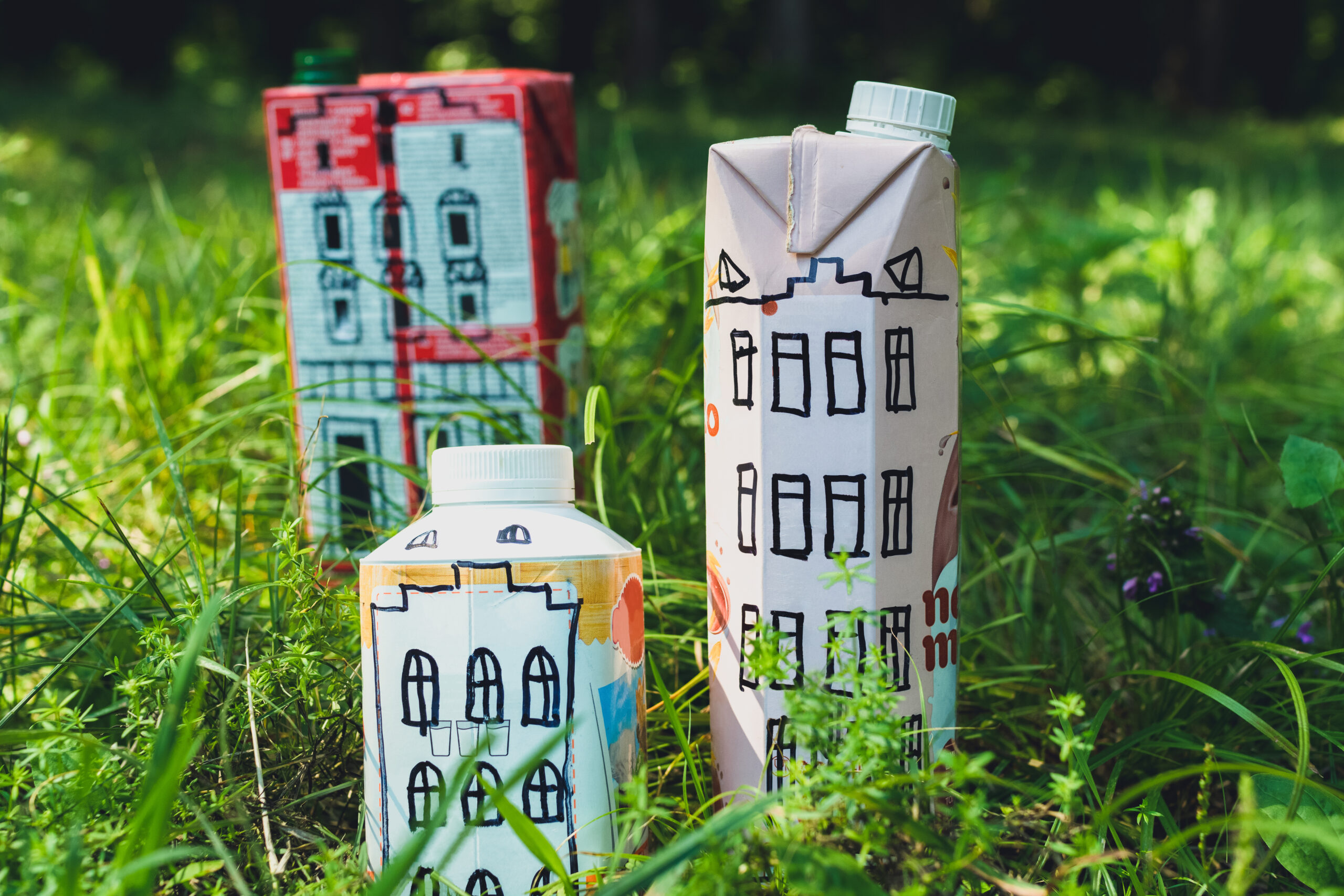 Houses and toy cars made from milk bags on grass. DIY paper milk bag. Creative paper milk bag ideas. Recycle crafts.